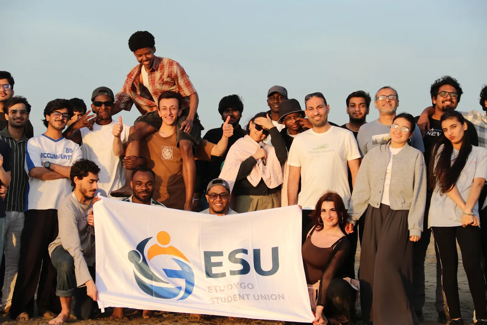 EtudyGo Student Union members holding the ESU banner on the beach at golden hour