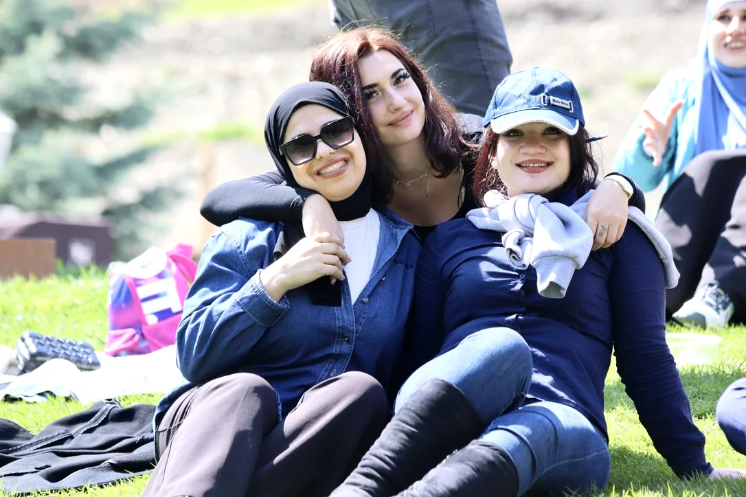 Three EtudyGo Student Union members sitting arm in arm on a sunlit lawn during the Azerbaijan trip