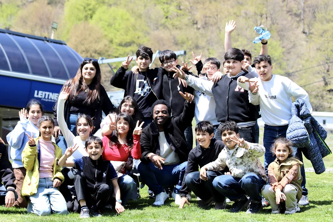EtudyGo Student Union members and younger family members crowded together on the grass, throwing peace signs, below the Gabala cable car